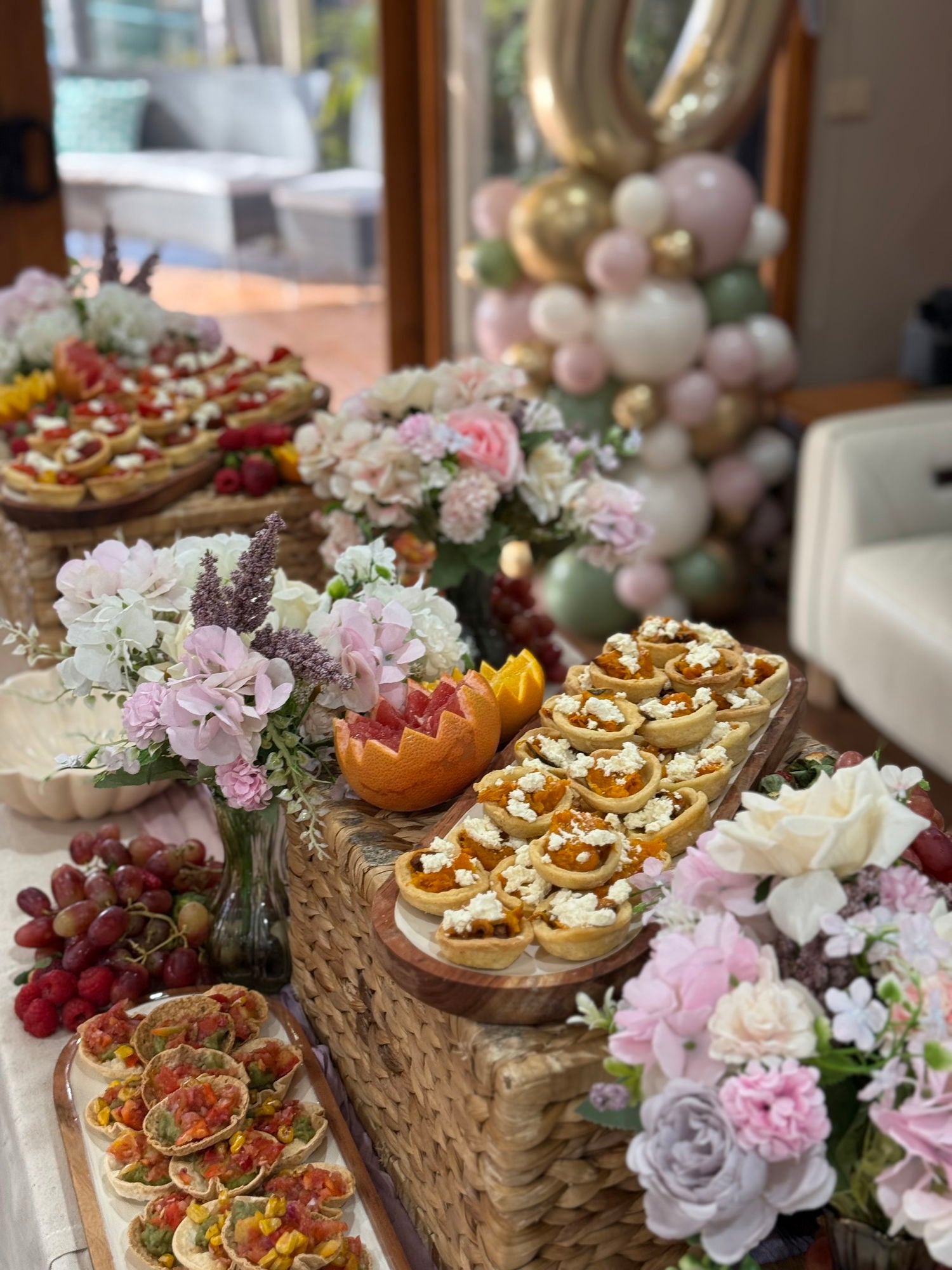Decorative table setting with appetizers, flowers, and balloons in a festive indoor setting.