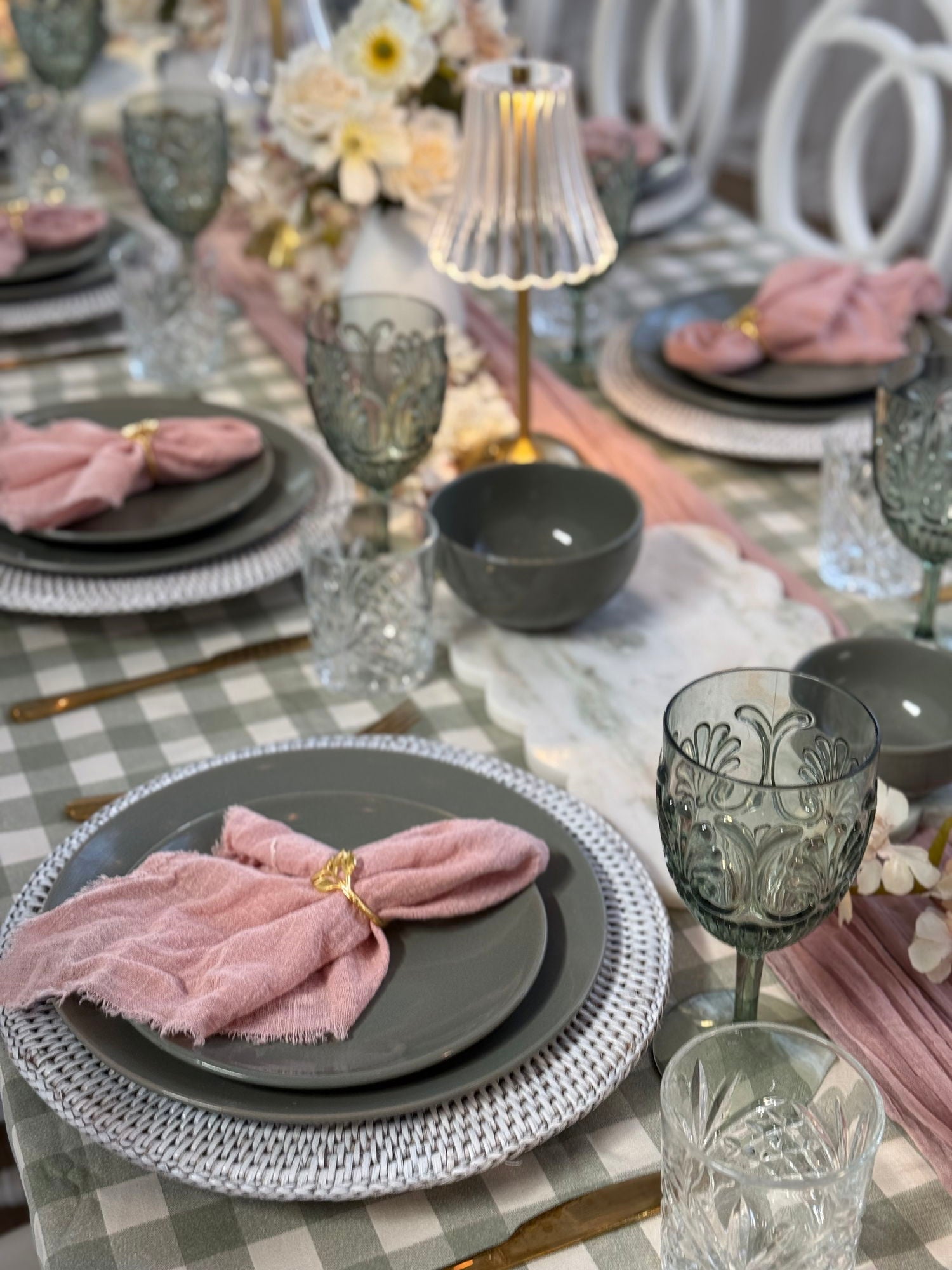 Elegant table setting with gray plates, pink napkins, and decorative glasses on a checkered tablecloth.