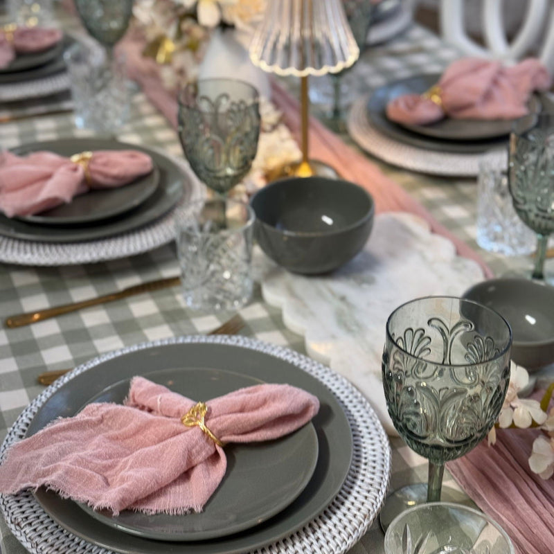 Elegant table setting with gray plates, pink napkins, and decorative glasses on a checkered tablecloth.